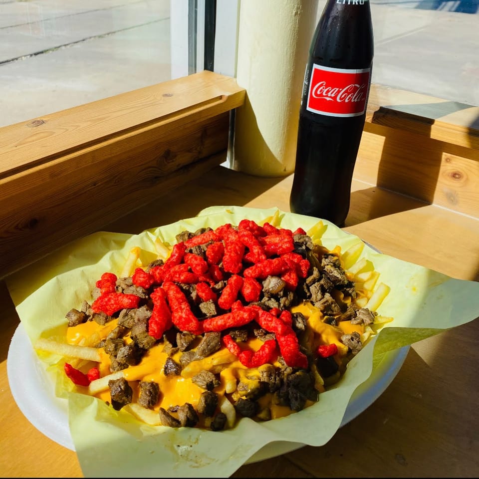 Wall St. Cocina's carne asada fries topped with cheese sauce and Hot Cheetos, with a Coca-Cola.