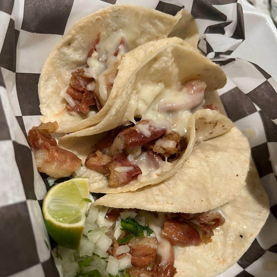 Three Wall St. Cocina tacos with meat, melted cheese, onions, cilantro, and a lime wedge.