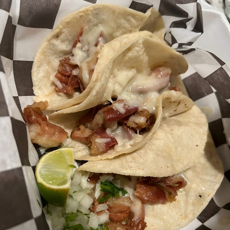 Three Wall St. Cocina tacos with meat, melted cheese, onions, cilantro, and a lime wedge.